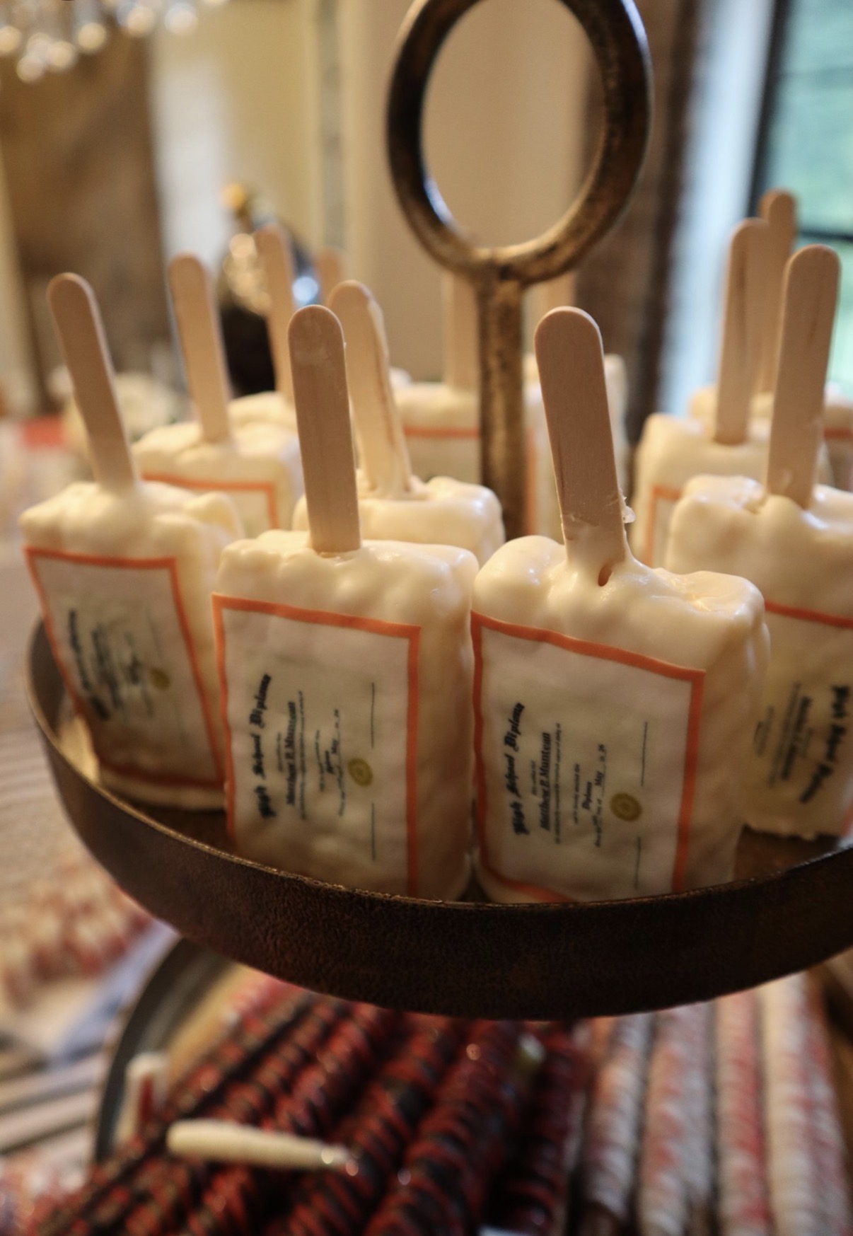 Tiered display of custom diploma cakesicles with red borders