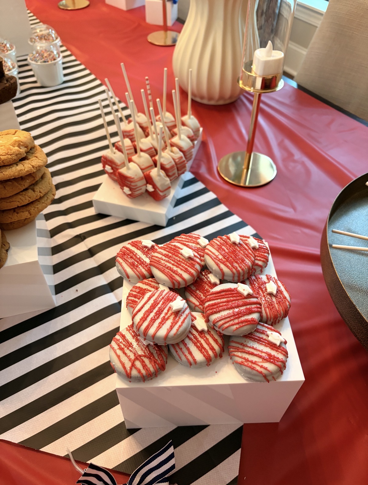 Red drizzle dipped Oreos and red cake pops on white display blocks