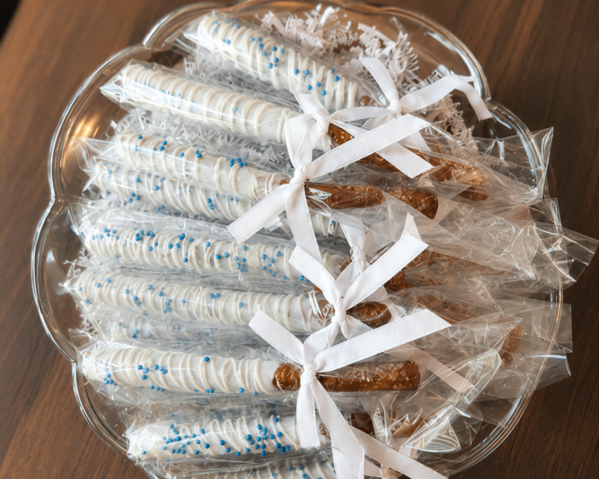 White chocolate pretzel rods with blue sprinkles arranged on a glass platter