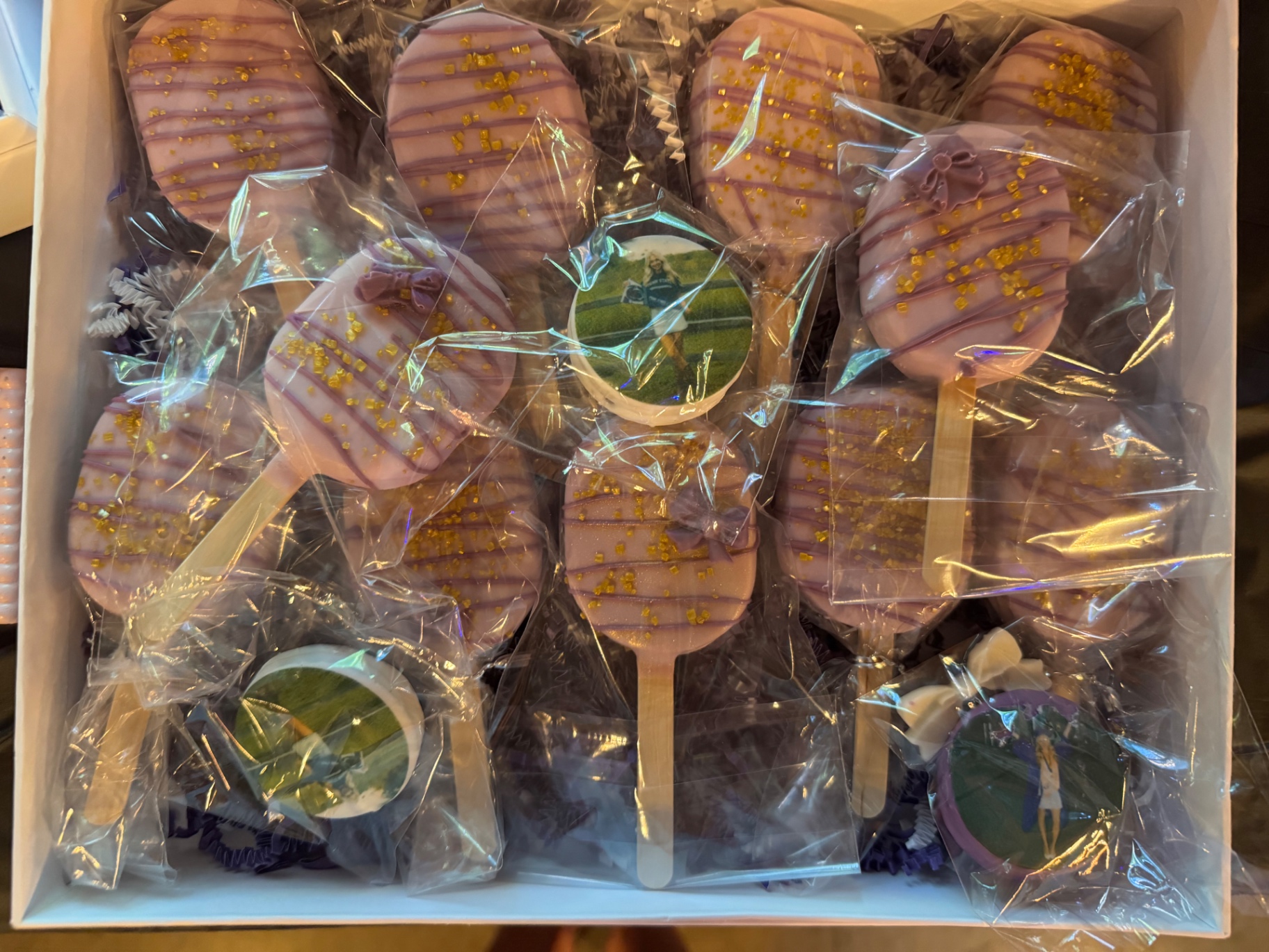 Box of purple and pink cakesicles with edible grad photos