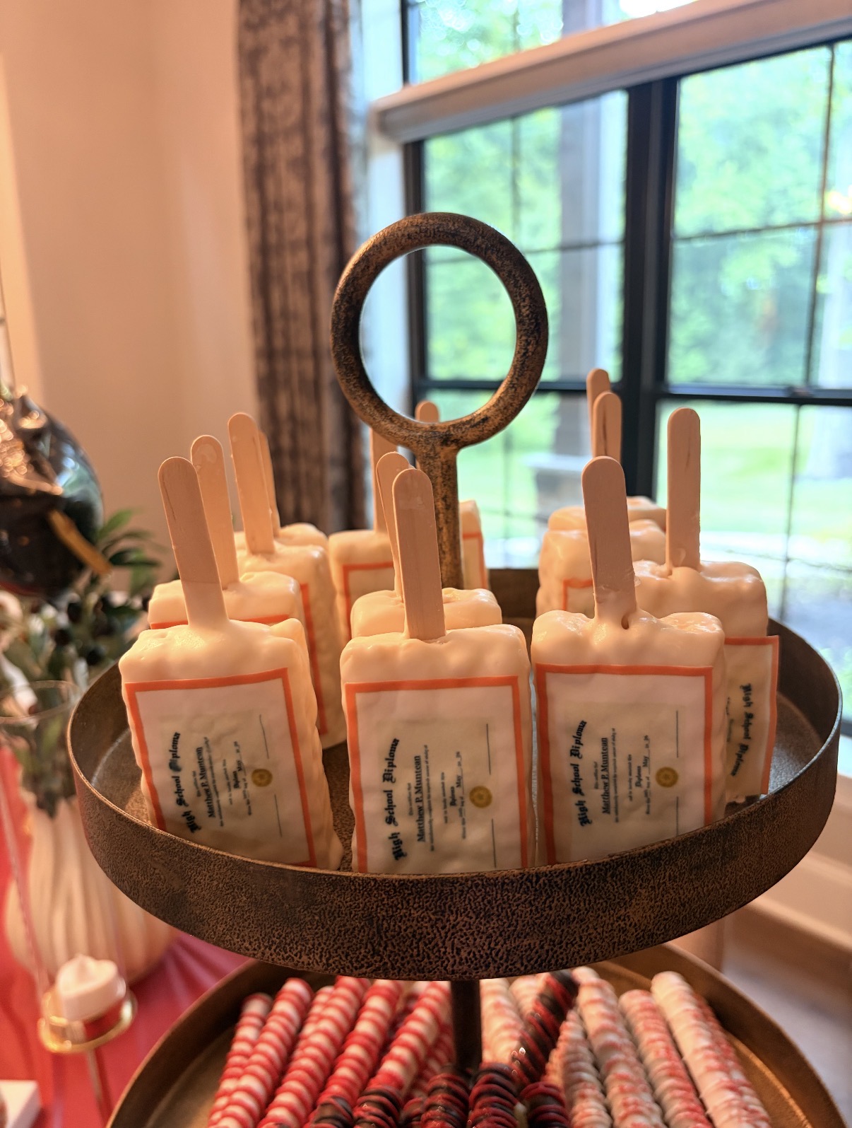 Tray of High School Diploma cakesicles with red and white pretzel rods below
